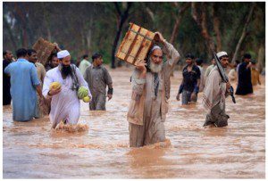 Residents and shopkeepers wade through a flooded street with their belongings after heavy rains in Peshawar on July 29. (Fayaz Aziz/Reuters - courtesy CBC.ca)