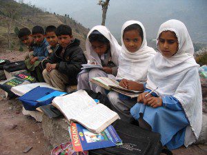 Kashmiri children sit in an outdoor classroom in the rubble of their former school. When weather is bad, the children don't attend school.