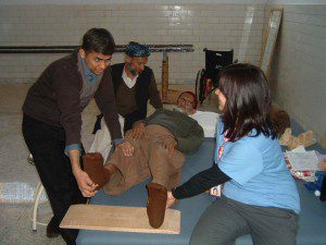 Sarah coaching local P.T., Rajeesh on stretching techniques for B.A. (75 y/o from Muzaffarabad with incomplete spinal cord injury).